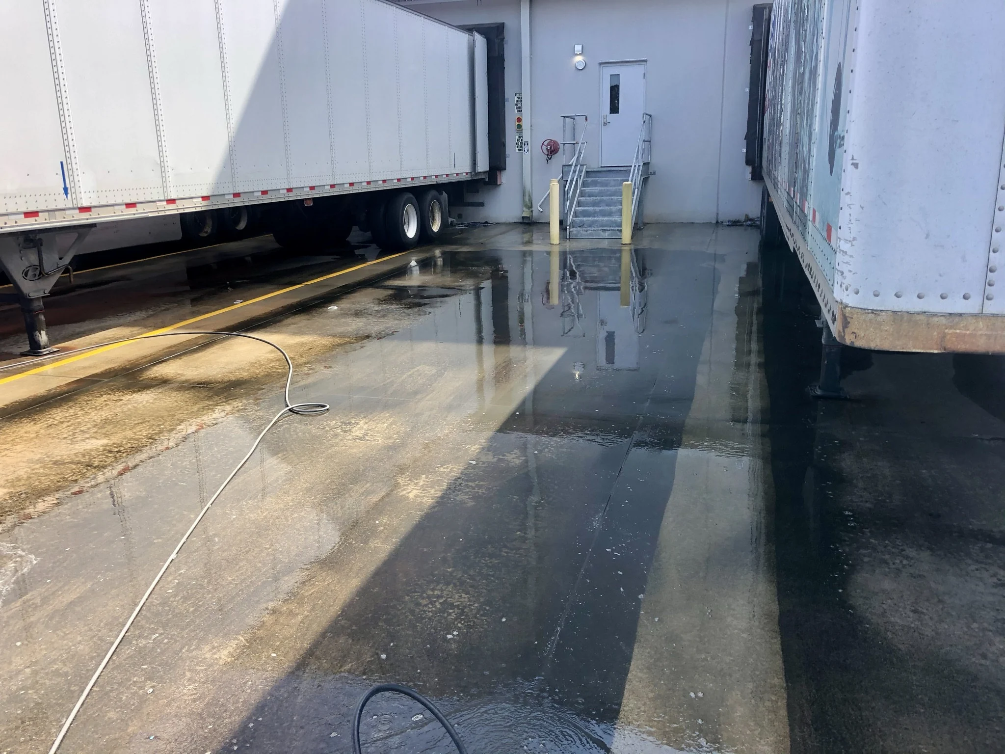 Commercial concrete loading dock lane wet with visible grime and residue between parked trailers